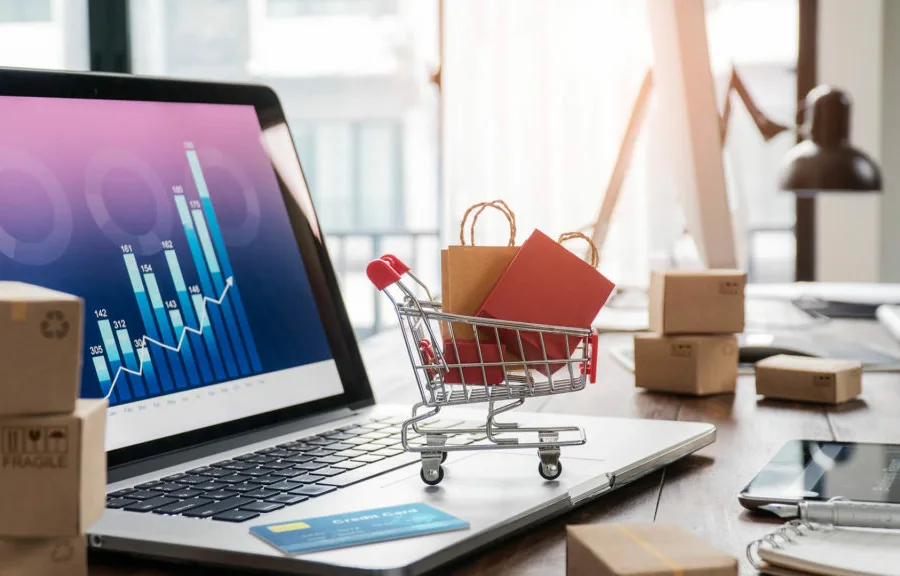 An open laptop with a tiny shopping cart perched about the mousepad.