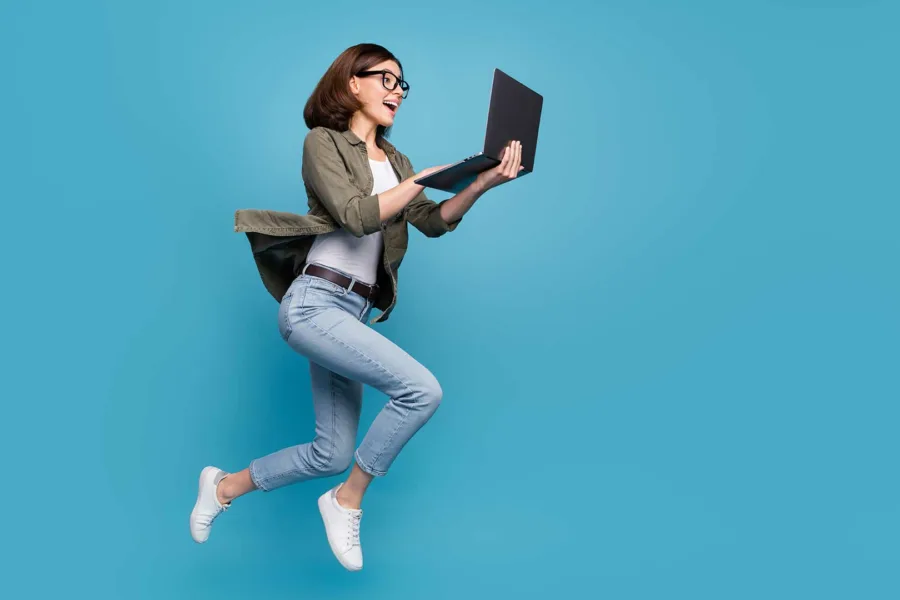 A woman jumping in the air while holding an open laptop