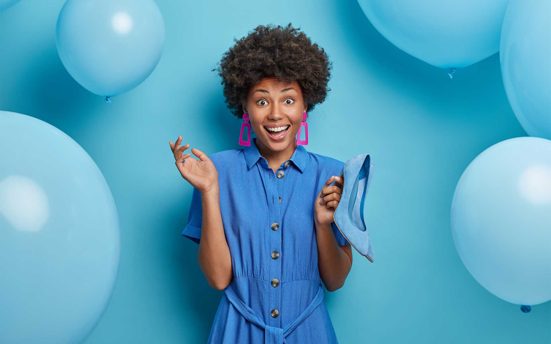A woman in blue smiling and standing against a blue backdrop